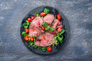 Modern style traditional Commonwealth Sunday roast with sliced cold cuts roast beef served with tomatoes and corn lettuce as top view on a Nordic design plate with copy space