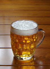 One glass mug with lager or porter is delicious frothy beer on a wooden tabletop a sunny day.