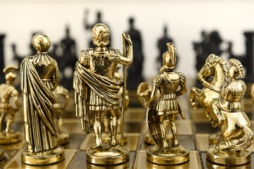 Fototapeta na wymiar Back of gold queen king centurion and knight chess piece figurines on chessboard facing black opposing army