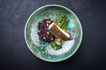 Modern style traditional fried skrei cod fish filet with baby broccoli, black rice and roasted pine...