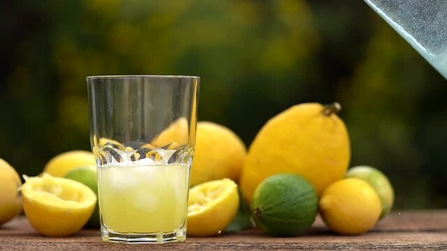 au ralenti,  quelqu'un verse de l'eau fra&icirc;che avec des gla&ccedil;ons dans un verre rempli  de jus de citron , le tout entour&eacute; d'agrumes