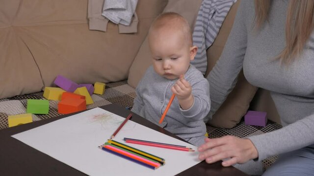 A little daughter enthusiastically drawings with colored pencils on sheet of paper, little girl next to her mother. Kid, son draws with colored pencils, boy is at home with his mother. Family and