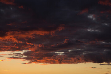 Epic dramatic sunset, sunrise on storm sky with dark clouds, orange yellow red sunlight

