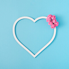 Creative layout made with white heart frame decorated with pink roses. Pastel blue background. Minimal love concept.