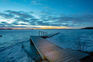 Winter sunrise over a lake covered with ice. Moon in the blue sky. Finland, Scandinavian nature