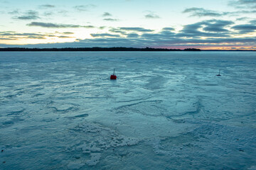 red mooring buoy and ice, snow structures on a frozen lake at sunrise in finland. scandinavian nature ук