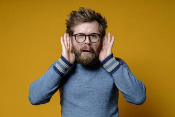 Strange hairy man tries something overheard having put hands to ears and with a bizarre expression...