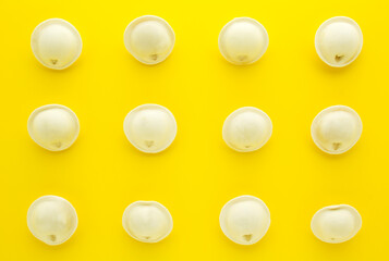 Uncooked frozen dumplings on yellow background.Russian pelmeni. Ravioli. Flat lay.
