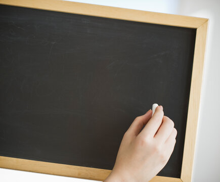Hand holding chalk in front of blank chalkboard