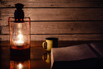 Un libro abierto y una taza de café a la luz de un candelabro por la noche.