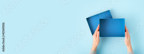 Female hands opening gift box isolated on blue background. Overhead view.