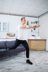 Fototapeta na wymiar Handsome sporty man in a T-shirt doing squats at home in his apartment. Fitness at home. Healthy lifestyle