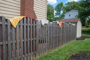 Colorful towels spread opened and hanging on a wooden fence near a backyard swimming pool on a sunny summer day