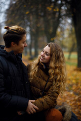 Fototapeta premium Caucasian guy with a girl laugh and smile looking at each other. young happy couple hugging in the park with yellow leaves on the background. friendship between a guy and a girl