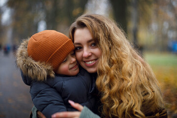 portrait of a young woman who smiles and hugs a child in warm clothes. young mother. mother's day...