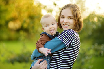 Fototapeta premium Cute big sister admiring her baby brother. Adorable teenage girl holding her new baby boy brother. Kids with large age gap. Big age difference between siblings.