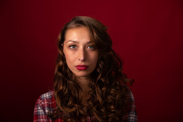 Close up portrait of Beautiful curly long hairy model in plaid shirt posing on red studio backdrop looking at camera. Pretty girl, women's beauty standards, cosmetics advertising copy space