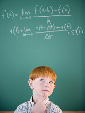Boy (8-9) calculating equation by blackboard