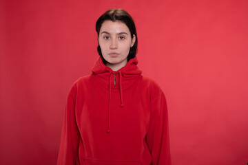 Fototapeta premium brunette Girl in red hoodie posing looking at camera duck lips on red studio backdrop copy space. Striving for gender neutrality, breaking gender stereotypes concept.