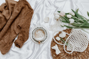 White tulip and coffee cup on silk background,  Morning coffee cup spring mood. Luxury romantic background. Top view, flat lay