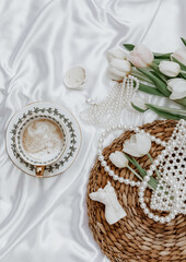 White tulips, coffee cup and woman accessory on silk background,  Morning coffee cup spring mood. Luxury romantic background. Woman morning, aesthetic concept. Top view, flat lay