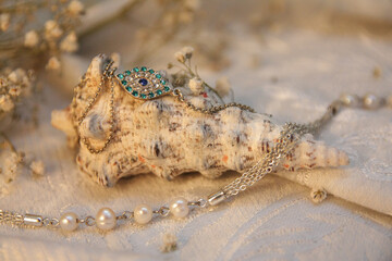 Ocean white shell with a blue eye-shaped jewelry bracelet on a vintage fabric with dried flowers and natural pearl beads.