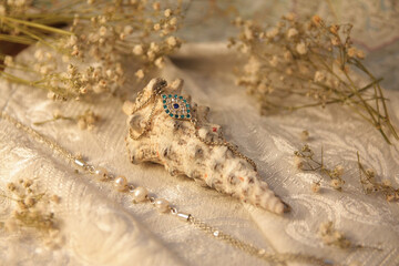 Ocean white shell with a blue eye-shaped jewelry bracelet on a vintage fabric with dried flowers and natural pearl beads.