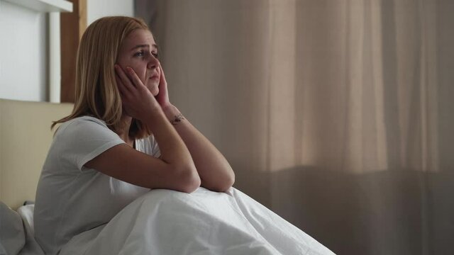 Morning anxiety. Female loneliness. Insomnia frustration. Disturbed depressed upset tired woman suffering from headache woke up in bed touching face feeling unwell in light bedroom.