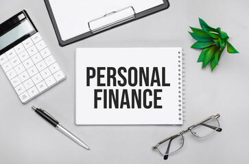 Writing text showing PERSONAL FINANCE. Calculator,pen,plan,glasses and black folder on grey background