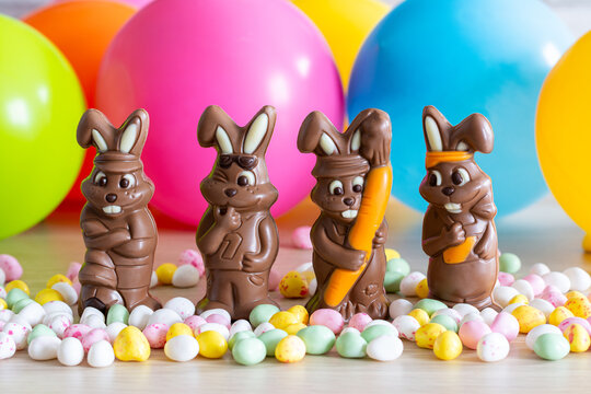 P&acirc;ques. Quatre petits lapins en chocolat au lait. Petits &oelig;ufs. Sur fond de ballons multicolores.
