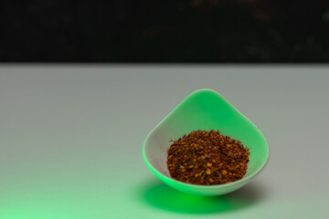 selective focus of a bowl with red cayenne pepper flakes with green light for contrast and background with copy space