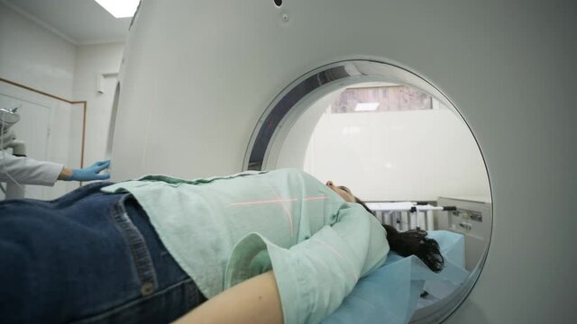 Female patient is undergoing CT or MRI scan under supervision of qualified radiologist in modern medical clinic. Patient lying on a CT or MRI scan table, moving outside the machine