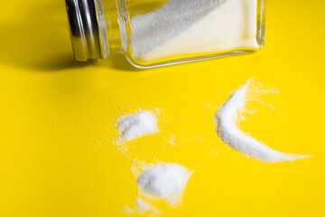 Sad face made of salt on a yellow background - the concept of the harm of salt to health