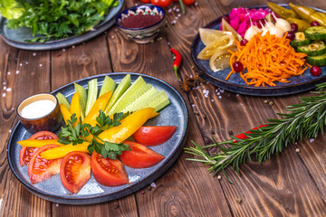 Pickled vegetables: peppers, carrots, garlic, cabbage lie on a platter on a wooden background decorated with chili peppers, cherry tomatoes, rosemary.