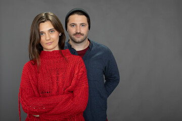 Beautiful casual dressed couple posing on grey background copy space. Pretty long-haired girl and Handsome unshaven guy in knitted cap looking at camera. romantic Family couple, marriage bonds concept