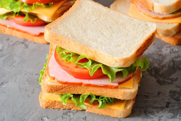 Tasty sandwiches with ham, salad, cheese and tomatoes on gray background, selective focus, close-up view