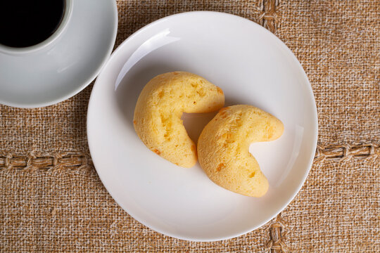 Two chipas or p&atilde;o de queijo or Brazilian bread in a white plate with a cup of coffee. Coffee break of breakfast. Isolatad, closeup.