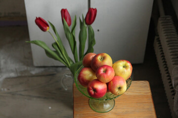 Still life, consisting of a bouquet of red tulips in a jug, a bowl of apples, a cup of tea and a bowl of coconut sweets.