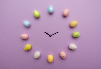 Colorful Easter eggs form a clock with clock hands in the middle on purple background. Spring holidays concept