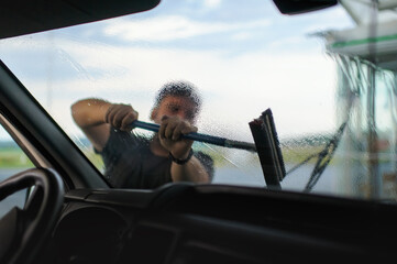 A view from inside a car of a male figure washing the windshield with a squeegee.