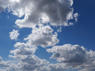 Blue sky with white clouds and the sun peeking out from behind them. Bright