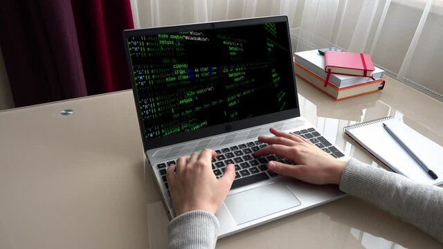 Source code on the monitor screen. The girl working at home office hands on keyboard.