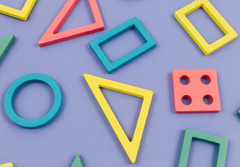 Multicolored wooden toys, blocks on violet background. Trendy puzzle toys. Geometric shapes: square, circle, triangle, rectangle. Educational toys for kindergarten, preschool or daycare. Close up