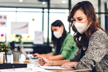 Young asian business woman using laptop computer working and planning meeting in quarantine for coronavirus wearing protective mask with social distancing while sitting on office desk