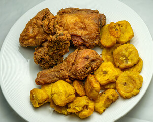 Fried chicken pieces on a bench served with fried plantains. Tostones, patacones, picapollo. 