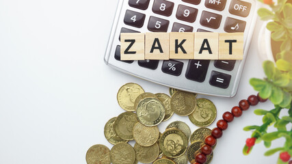 Islamic financial and banking concept. Top view of calculator, coins, prayer beads and wood blocks with word "ZAKAT". Copy space
