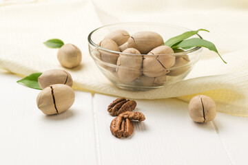 Pecans in a glass bowl on a piece of cloth on a white wooden table.