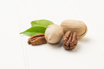 Two leaves, peeled and unpeeled pecans on a white wooden table.