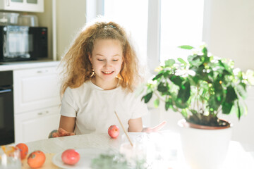 Cute tween girl with long curly hair painting eggs on kitchen at home on the spring sunny day, Happy Easter