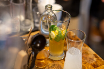 A close-up of a lemon-soda cold drink in a clear glass on the cafe table where the barista is mixing something into the glass. Summer refreshing drink